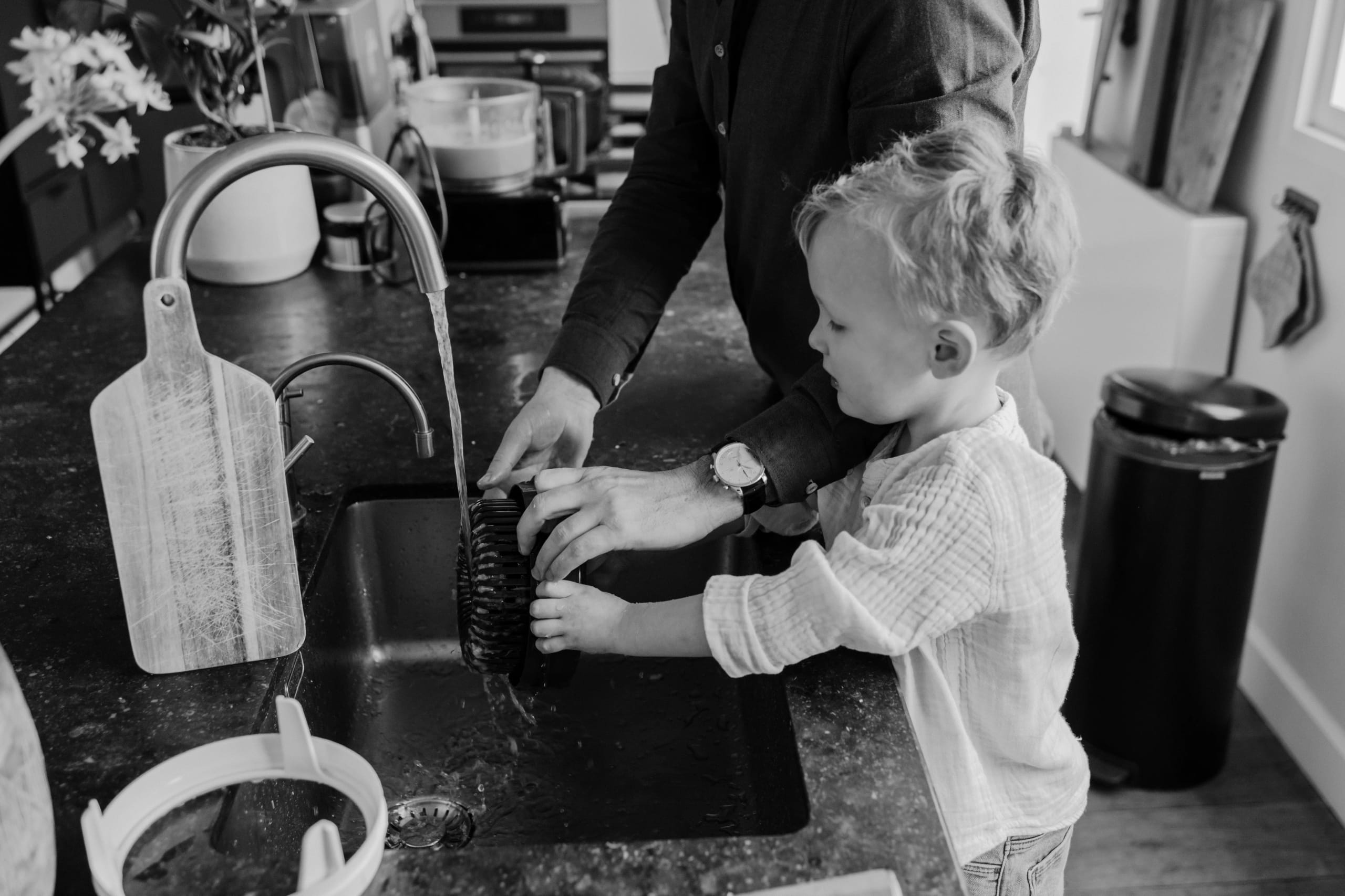 Zwart-wit beeld van een peuter die helpt met de afwas, pure lifestyle fotografie door Denise B Photography.