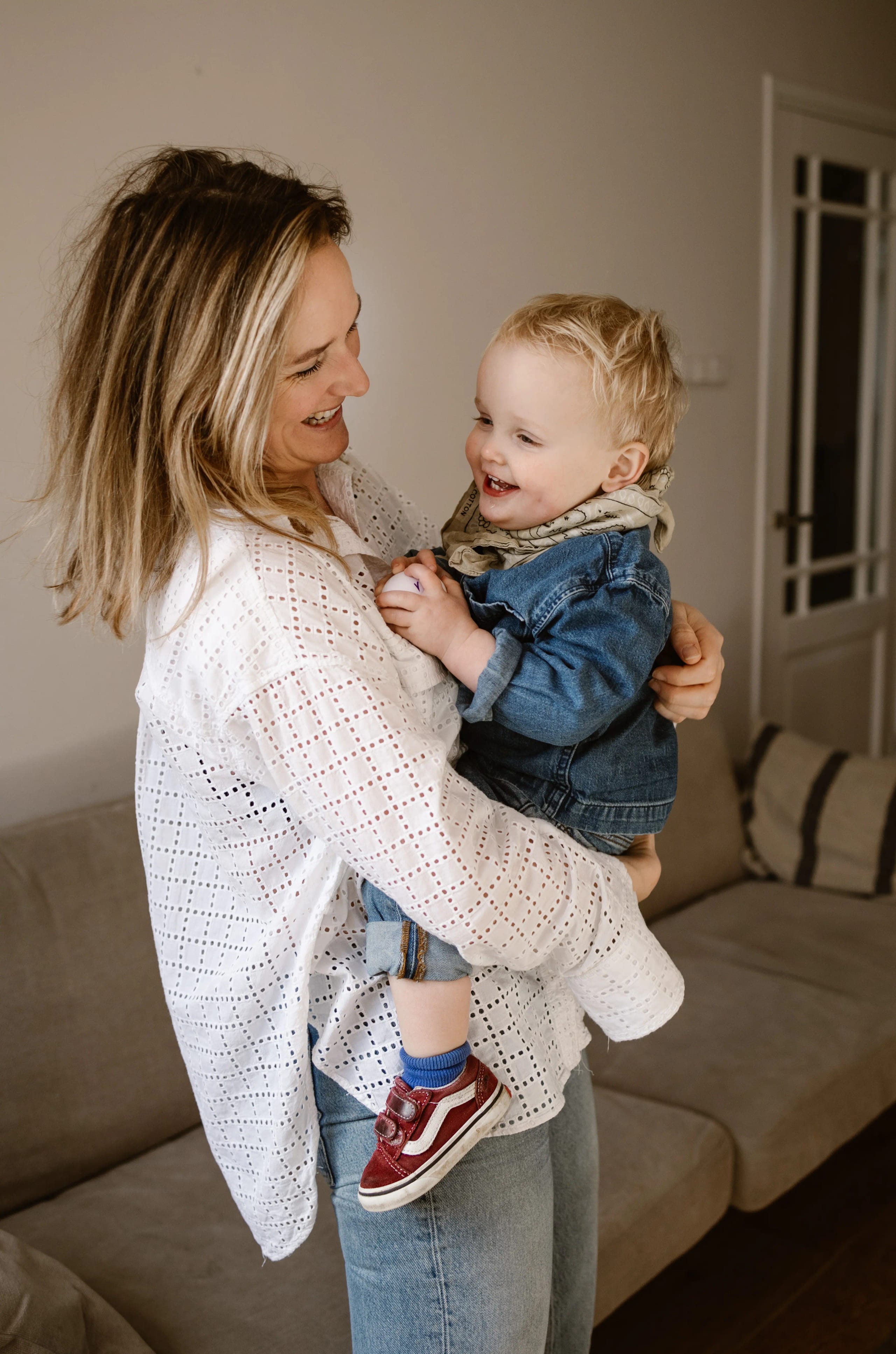 Moeder en kind lachen samen op de bank tijdens een lifestyle fotoshoot thuis.