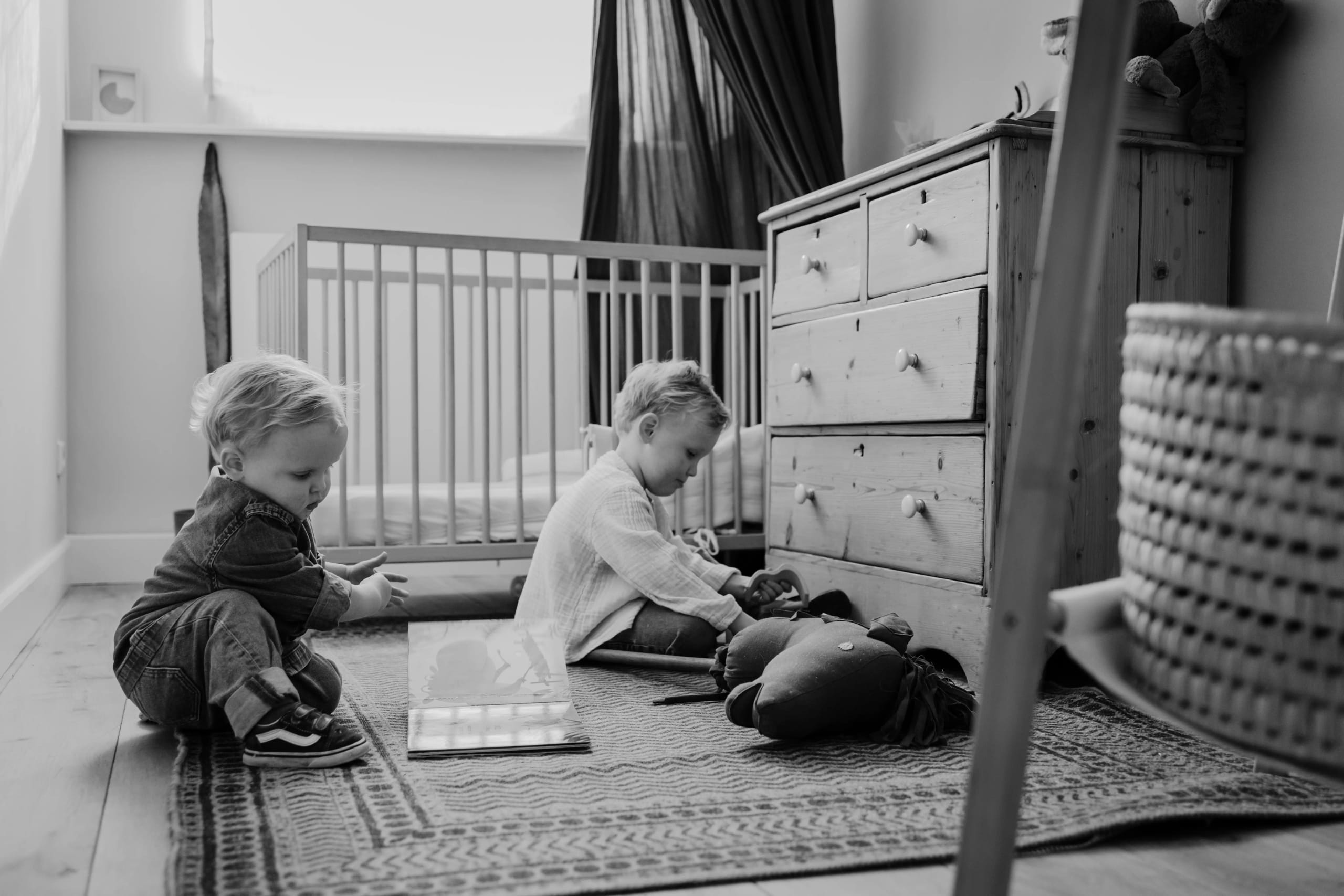 Zwart-wit foto van kinderen die spelen op de grond van hun slaapkamer, spontane momenten.