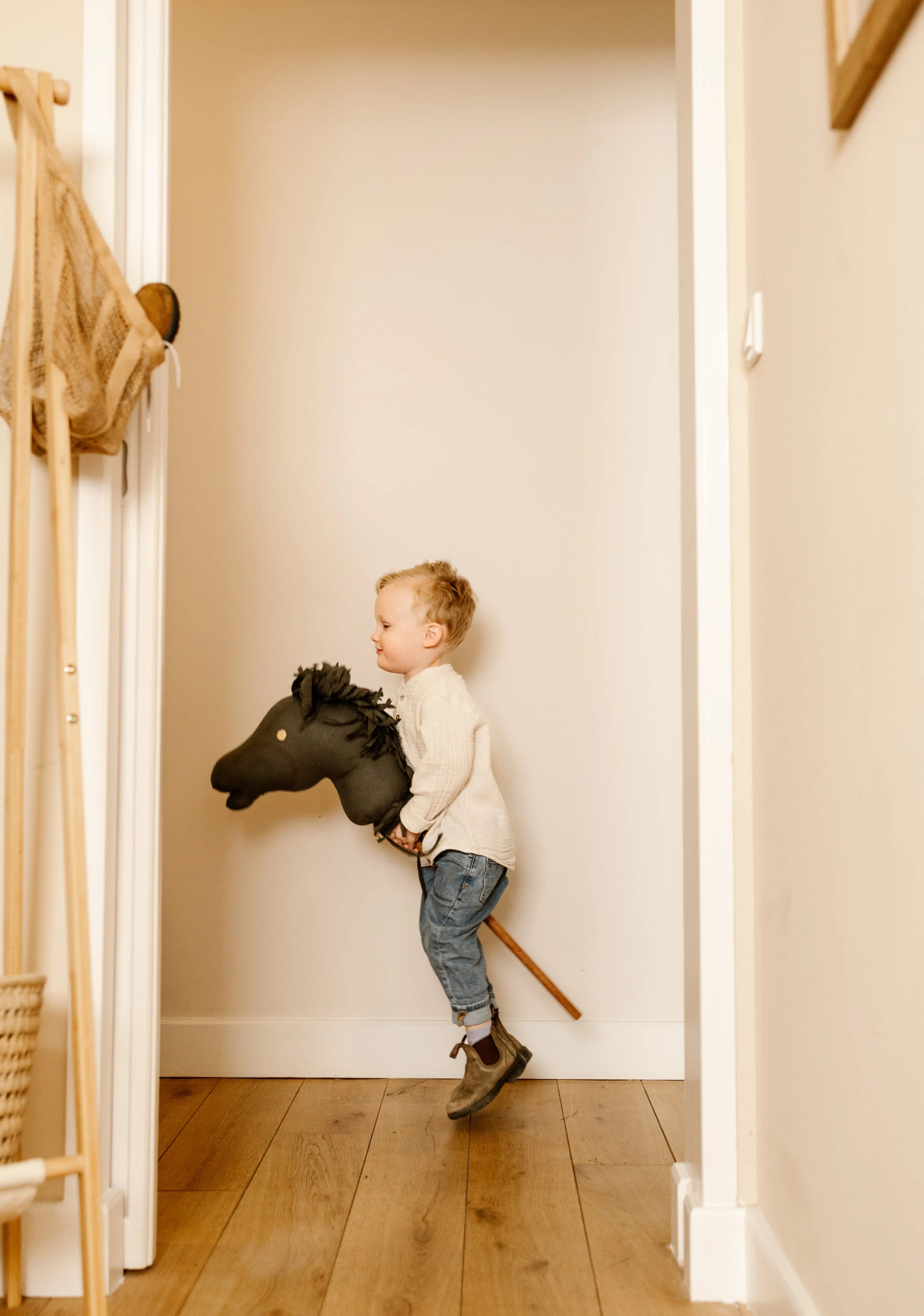 Peuter rijdt op een stokpaardje door de gang, creatieve kinderfotografie aan huis.