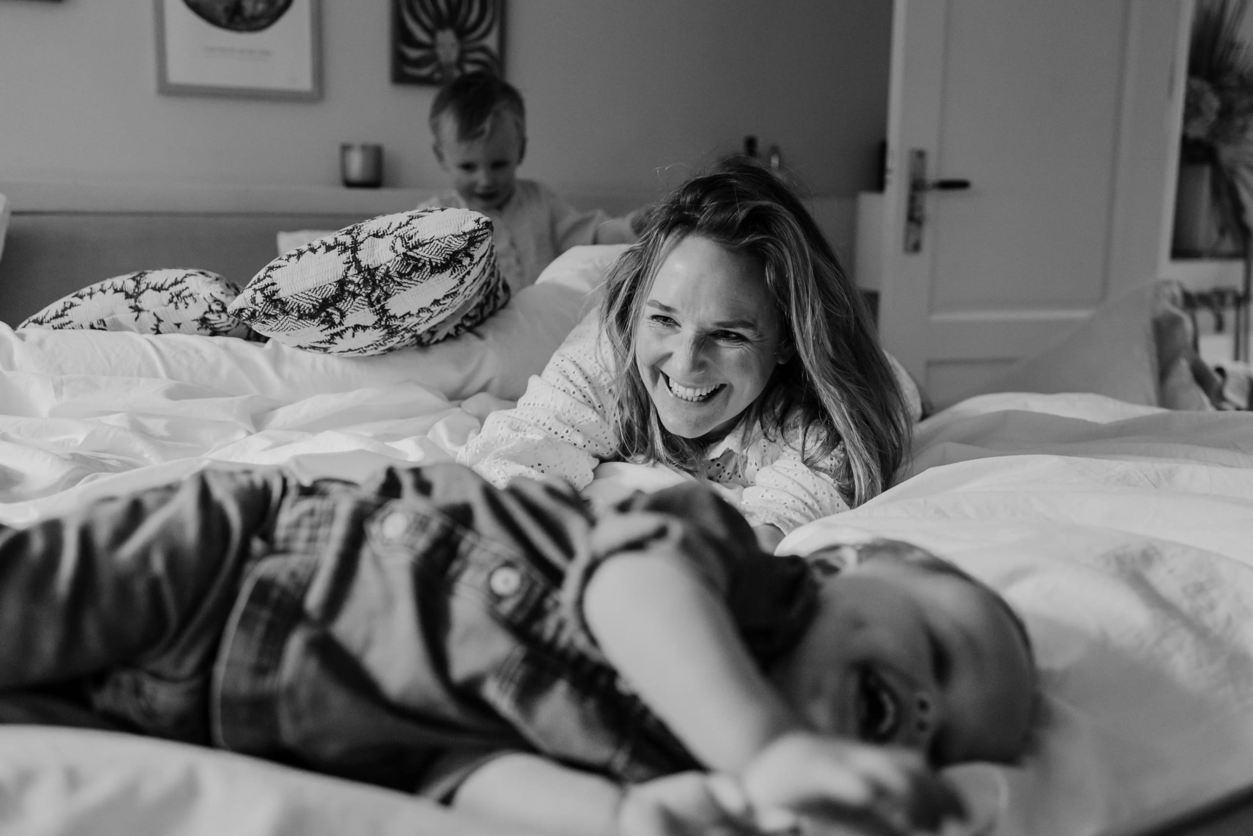 Zwart-wit portret van een moeder en kind die samen plezier maken op bed.