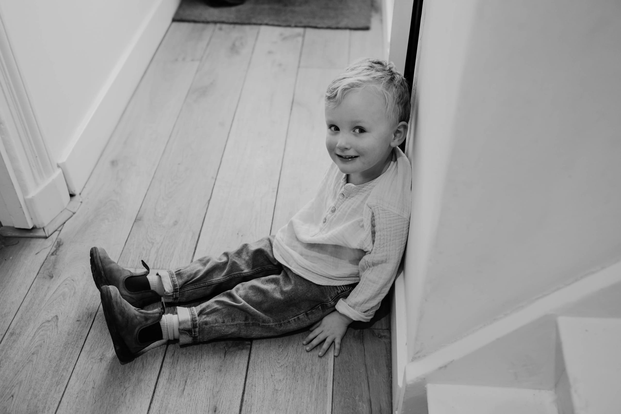 Zwart-wit foto van een peuter die rustig op de houten vloer zit, artistieke kinderfotografie.