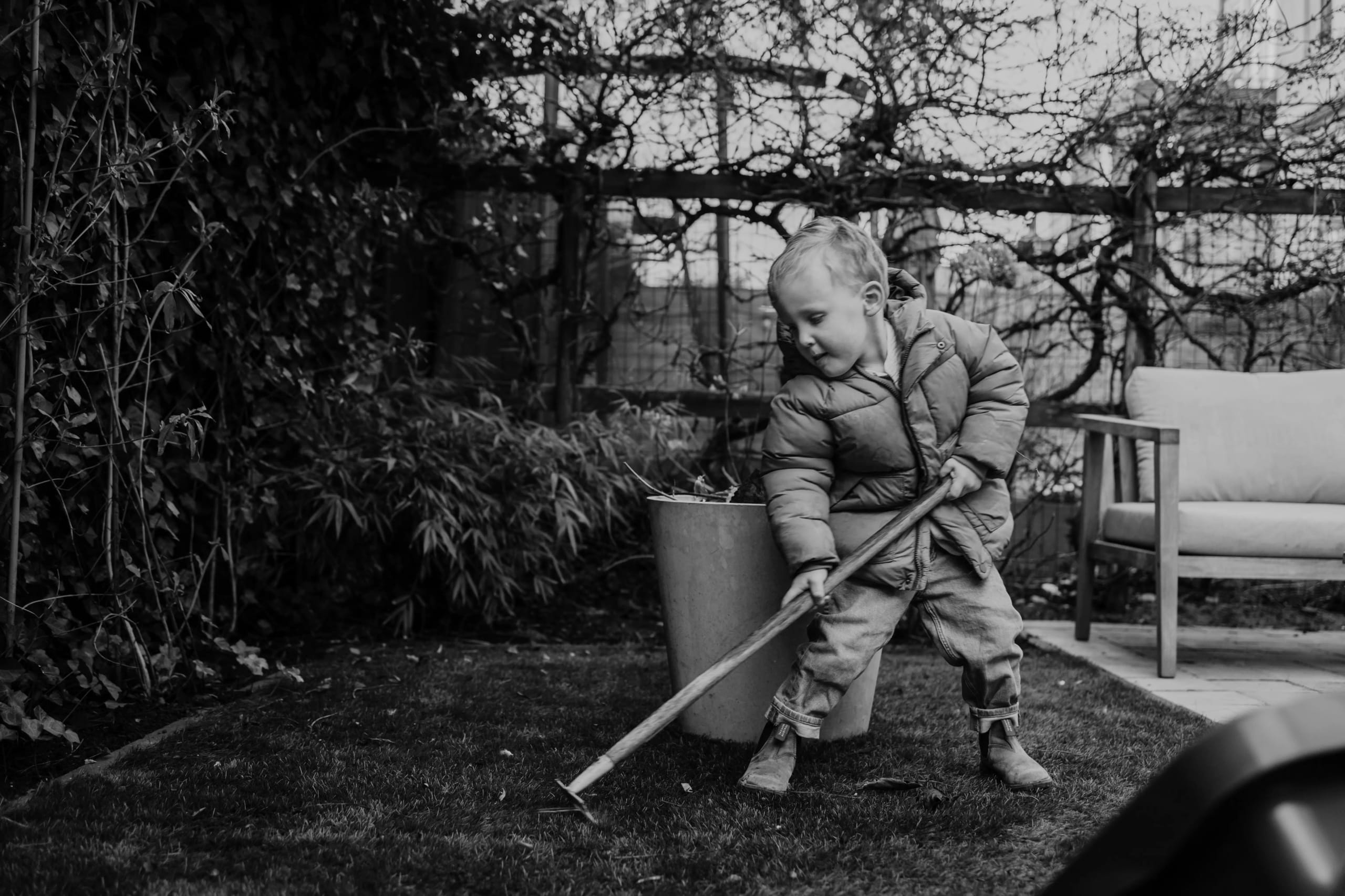 Zwart-wit beeld van een peuter die in de tuin werkt met een harkje.