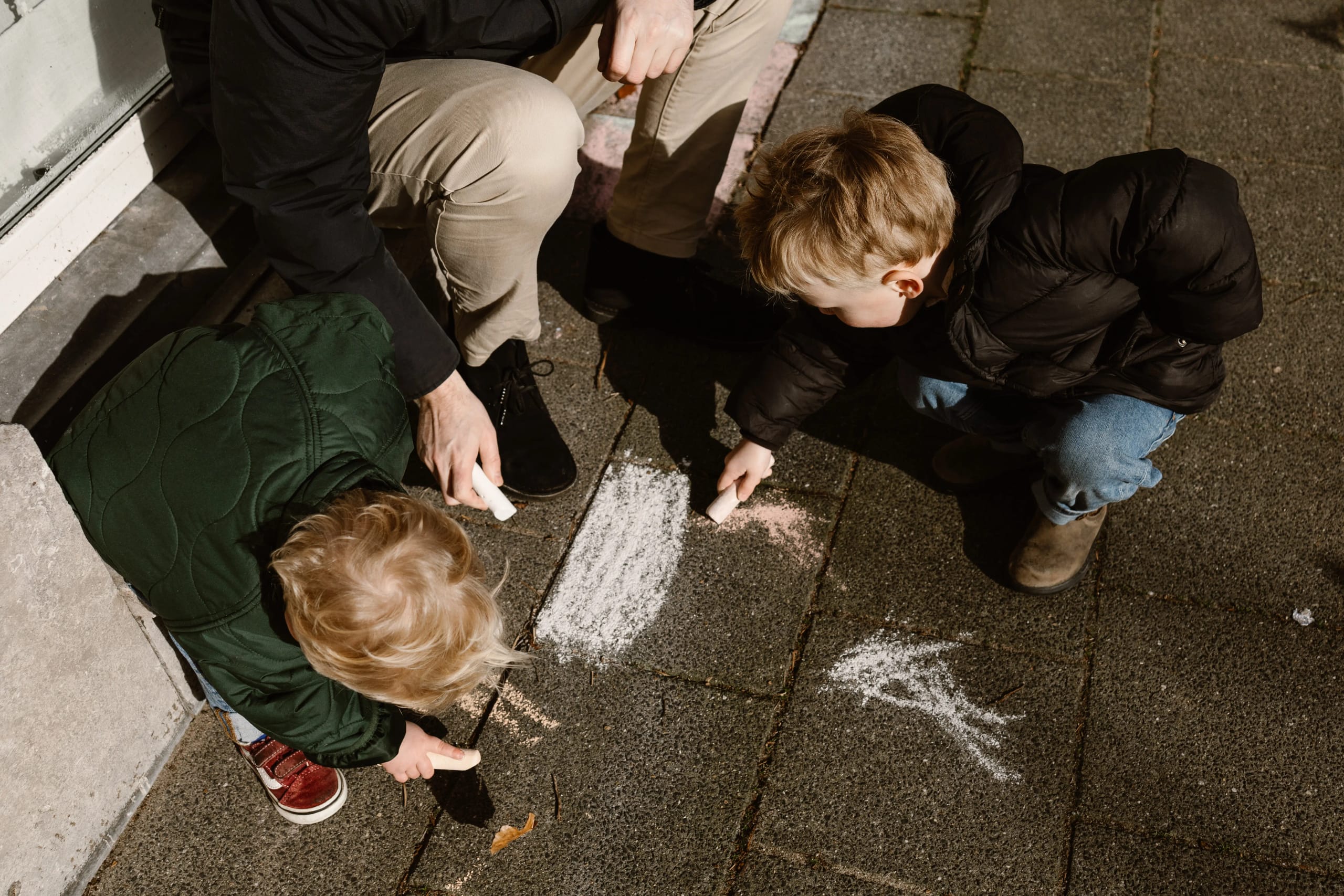 Vader en kind tekenen met stoepkrijt op de tegels, alledaagse momenten als herinnering.