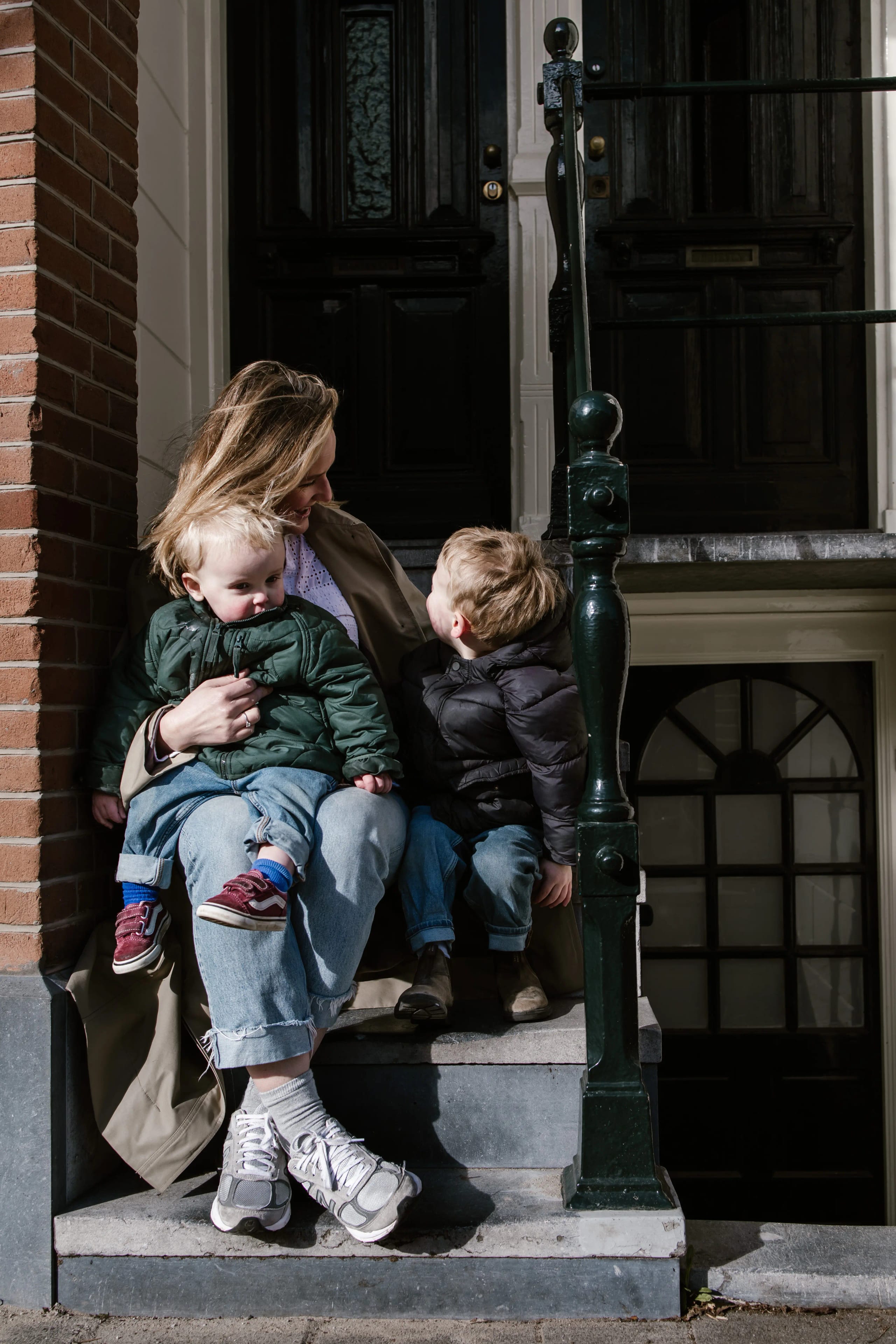 Moeder met haar twee kinderen op de trap van hun huis, authentiek familieportret.