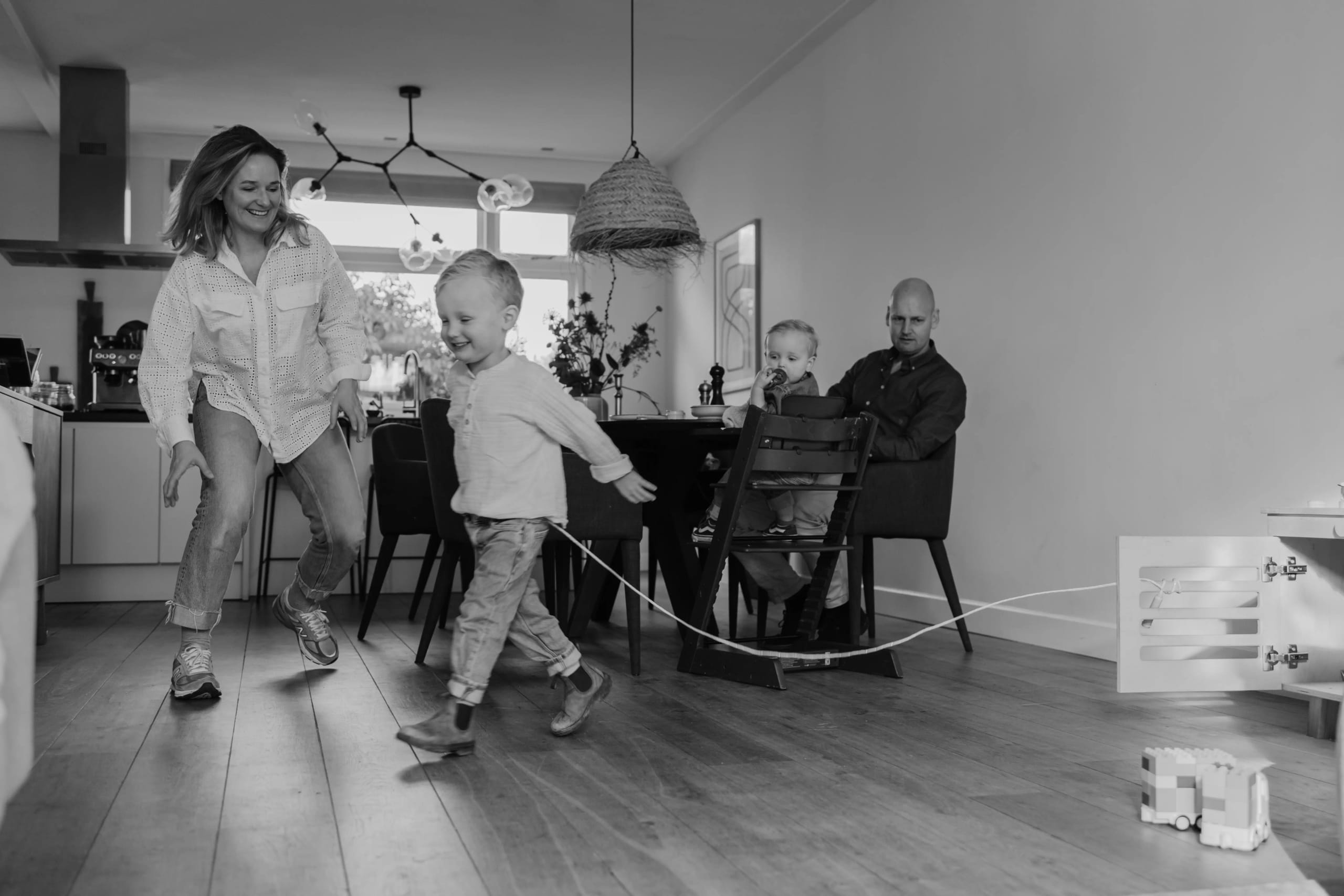 Gezinsleven in de keuken: een rennend kind en ouders aan tafel, zwart-wit lifestyle.
