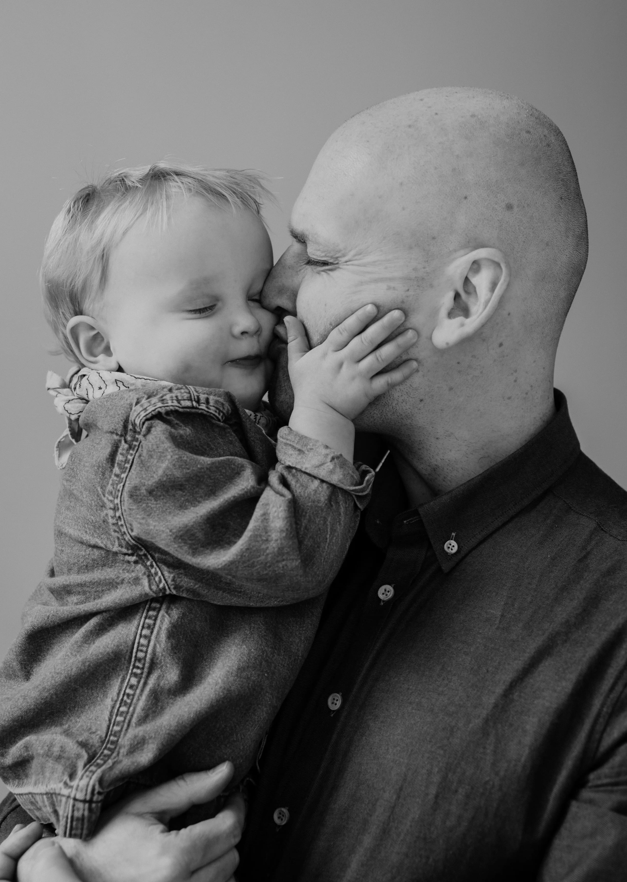 Vader geeft een kus op de wang van zijn kind, liefdevolle zwart-wit fotografie.