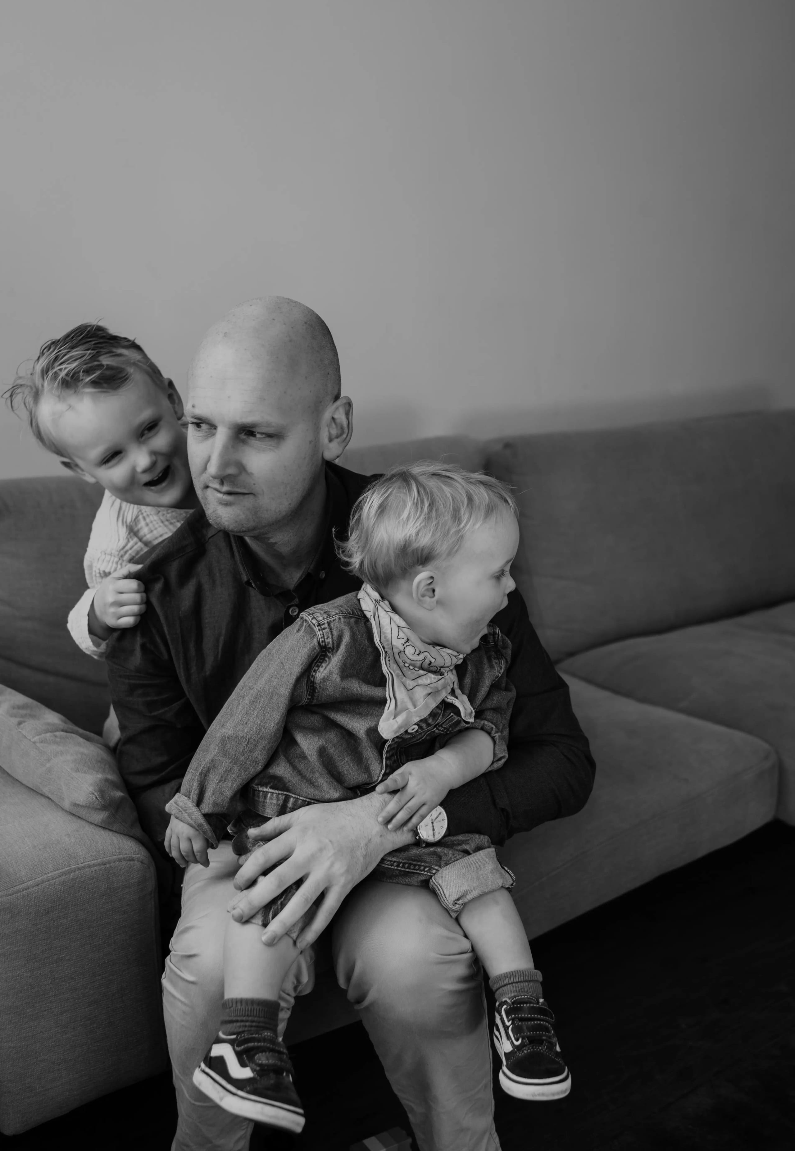 Vader zit met zijn twee zonen op de bank, pure en ongedwongen gezinsfoto.