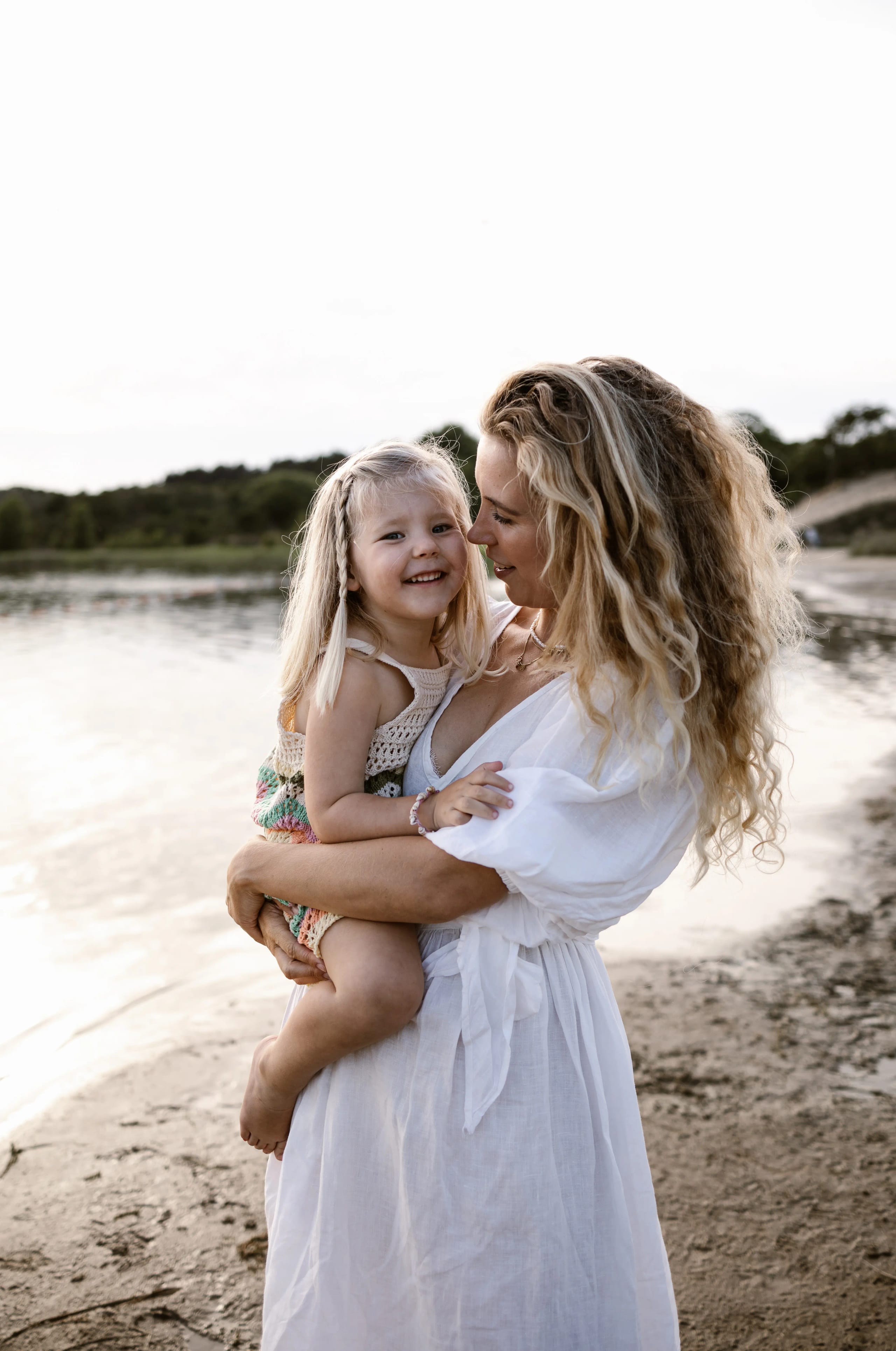 Moeder knuffelt haar dochter teder op het strand van Bloemendaal met de zee op de achtergrond.