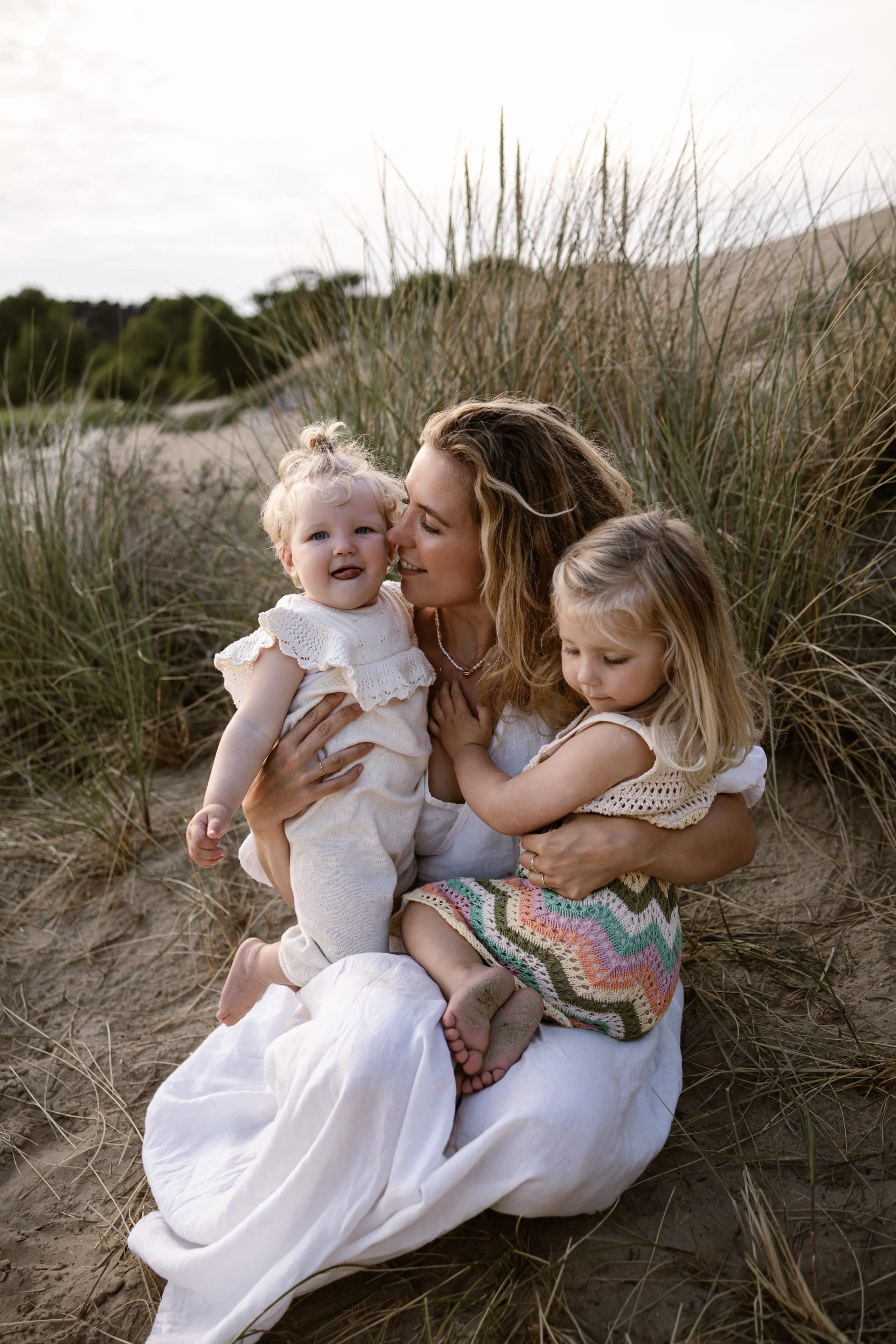 Moeder geeft haar kind een kus op de wang in het hoge duingras van Nationaal Park Zuid-Kennemerland.