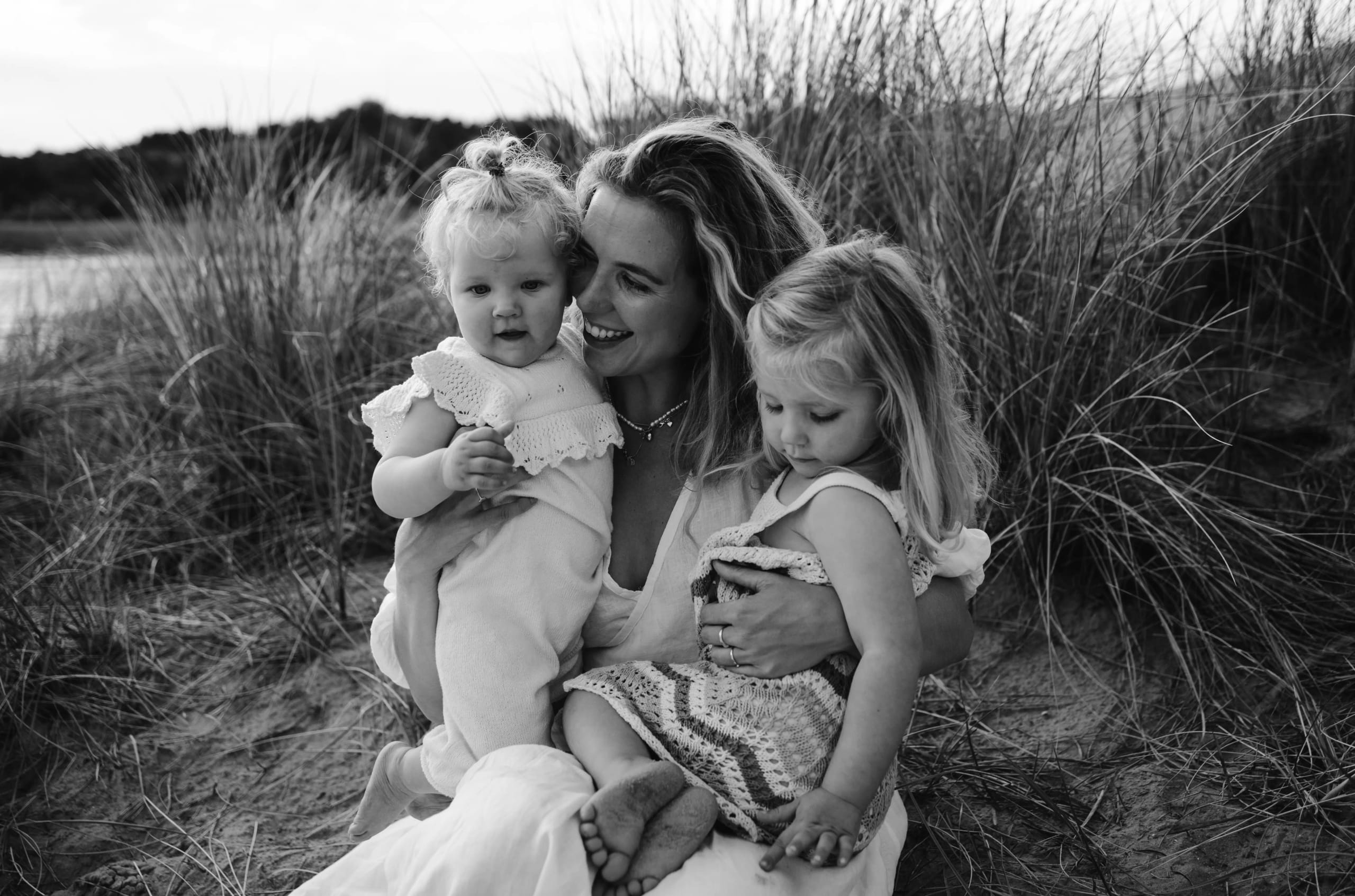 Zwart-wit foto van een moeder met haar twee kinderen in de Kennemerduinen, pure emotie en verbinding.