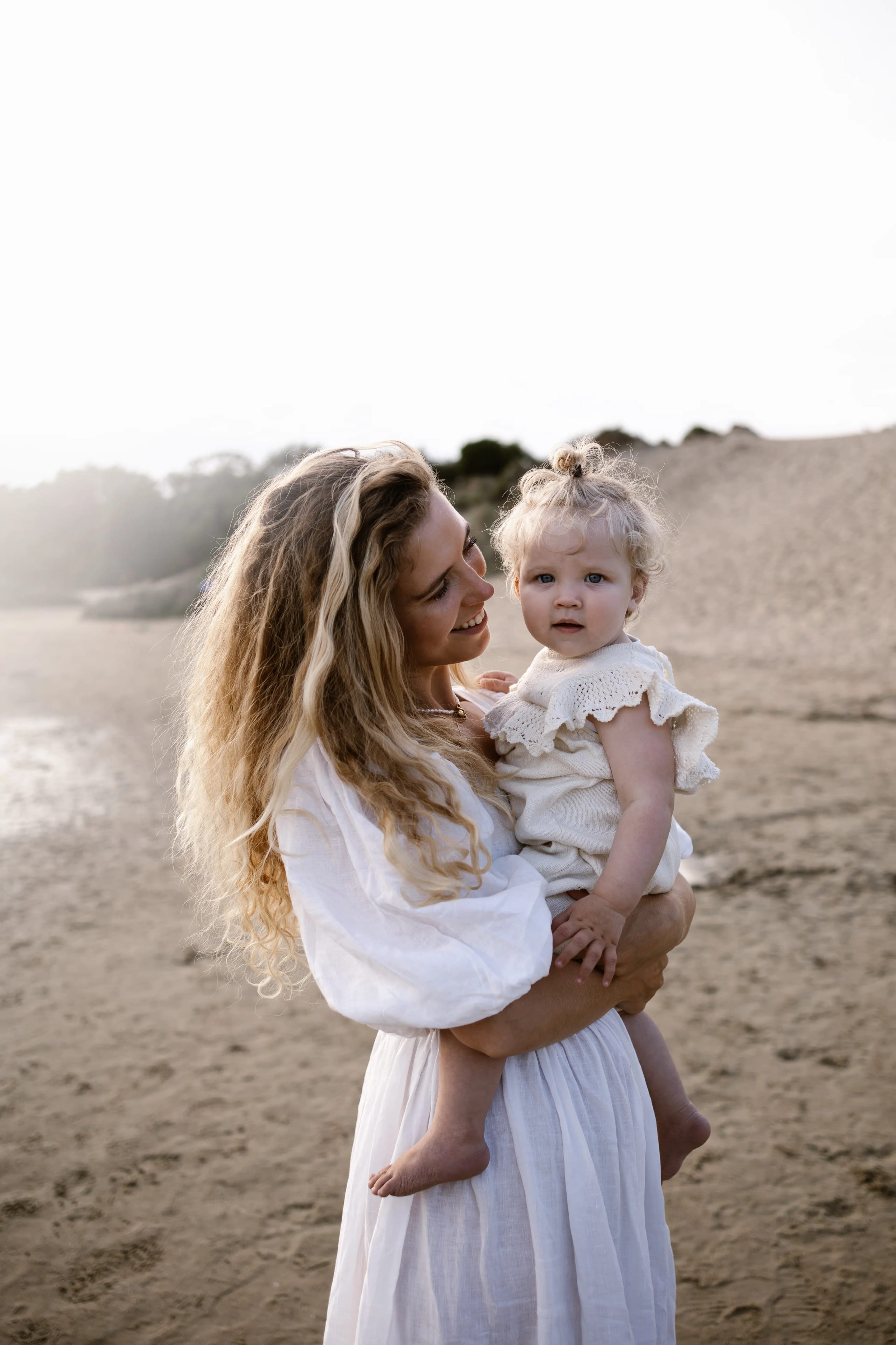 Moeder houdt haar kind omhoog tegen de zon in op het strand van Bloemendaal, magisch tegenlicht moment.