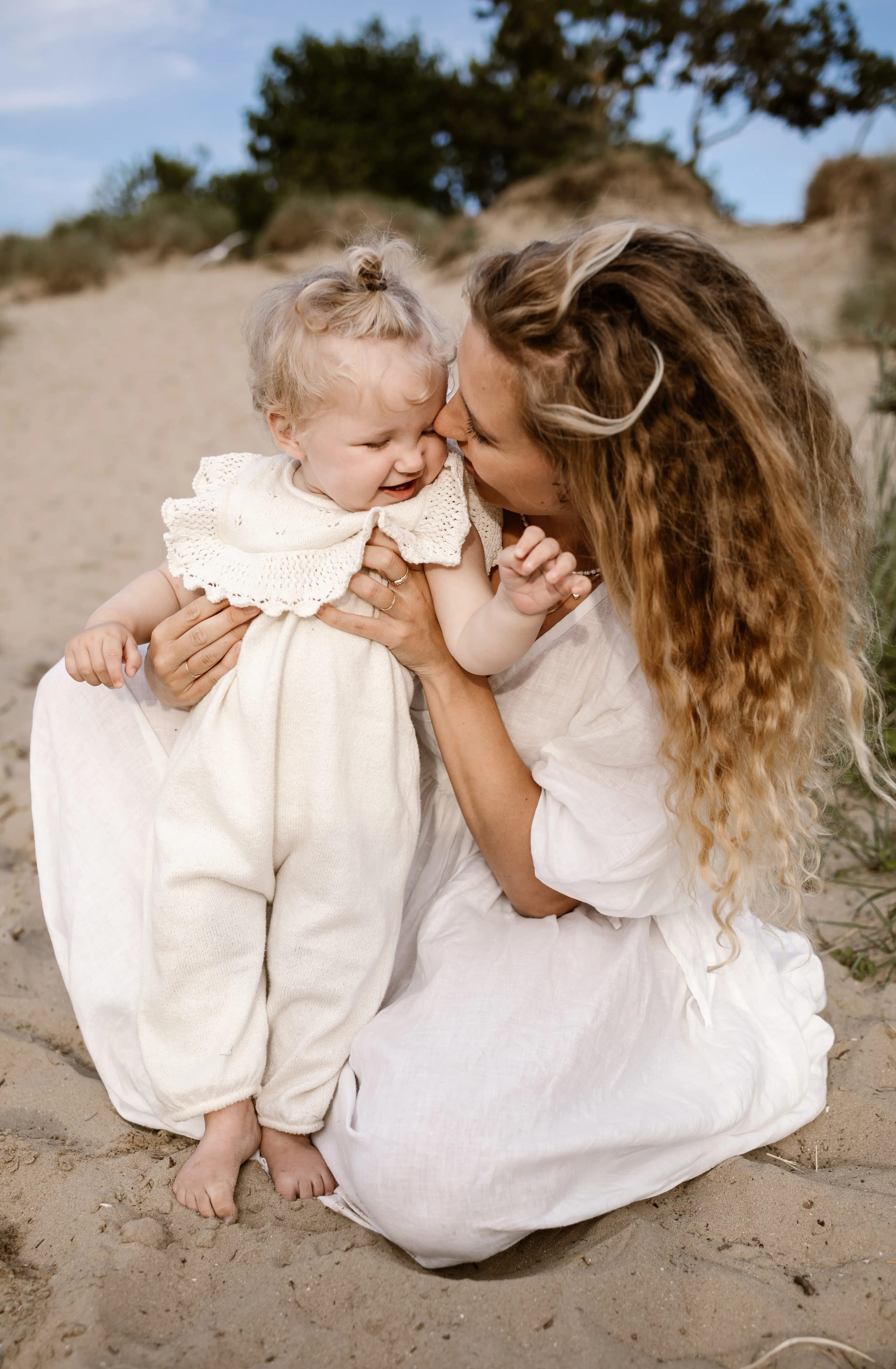 Moeder lacht samen met haar kind in het zand van de Bloemendaalse duinen, natuurlijke lifestyle beelden.