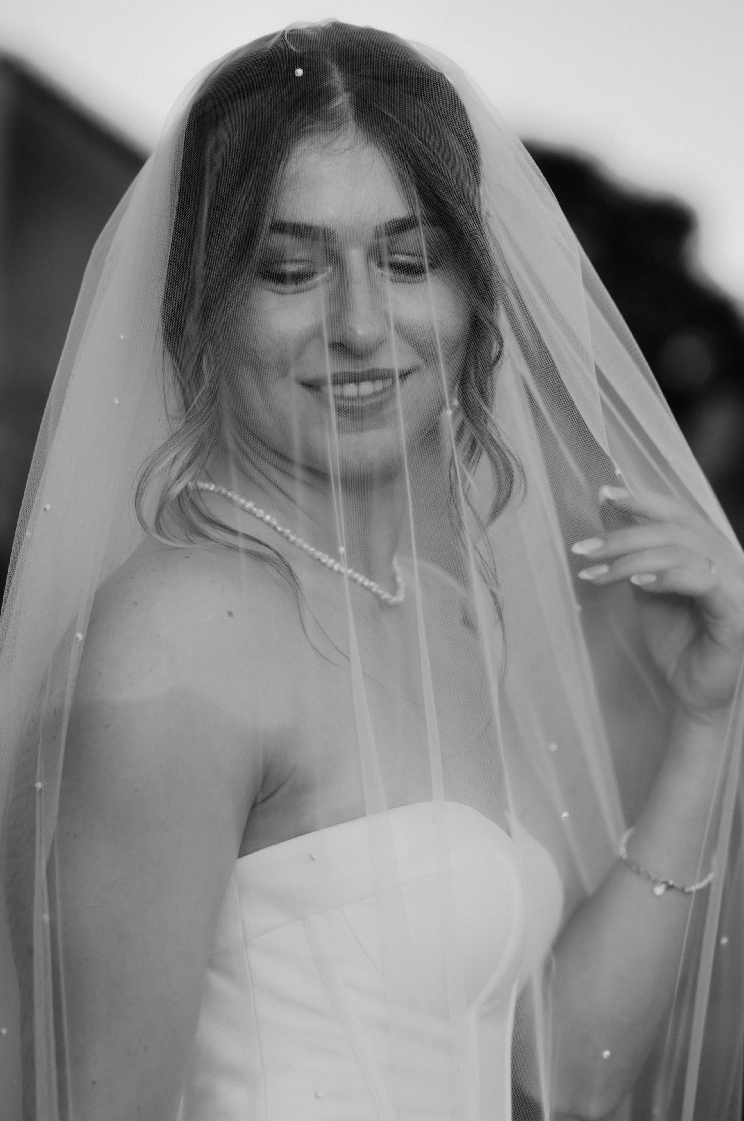 Een stralende bruid in een elegante strapless trouwjurk, met een delicate sluier en parelsieraden, die een zachte glimlach toont terwijl ze zich voorbereidt op haar grote dag.