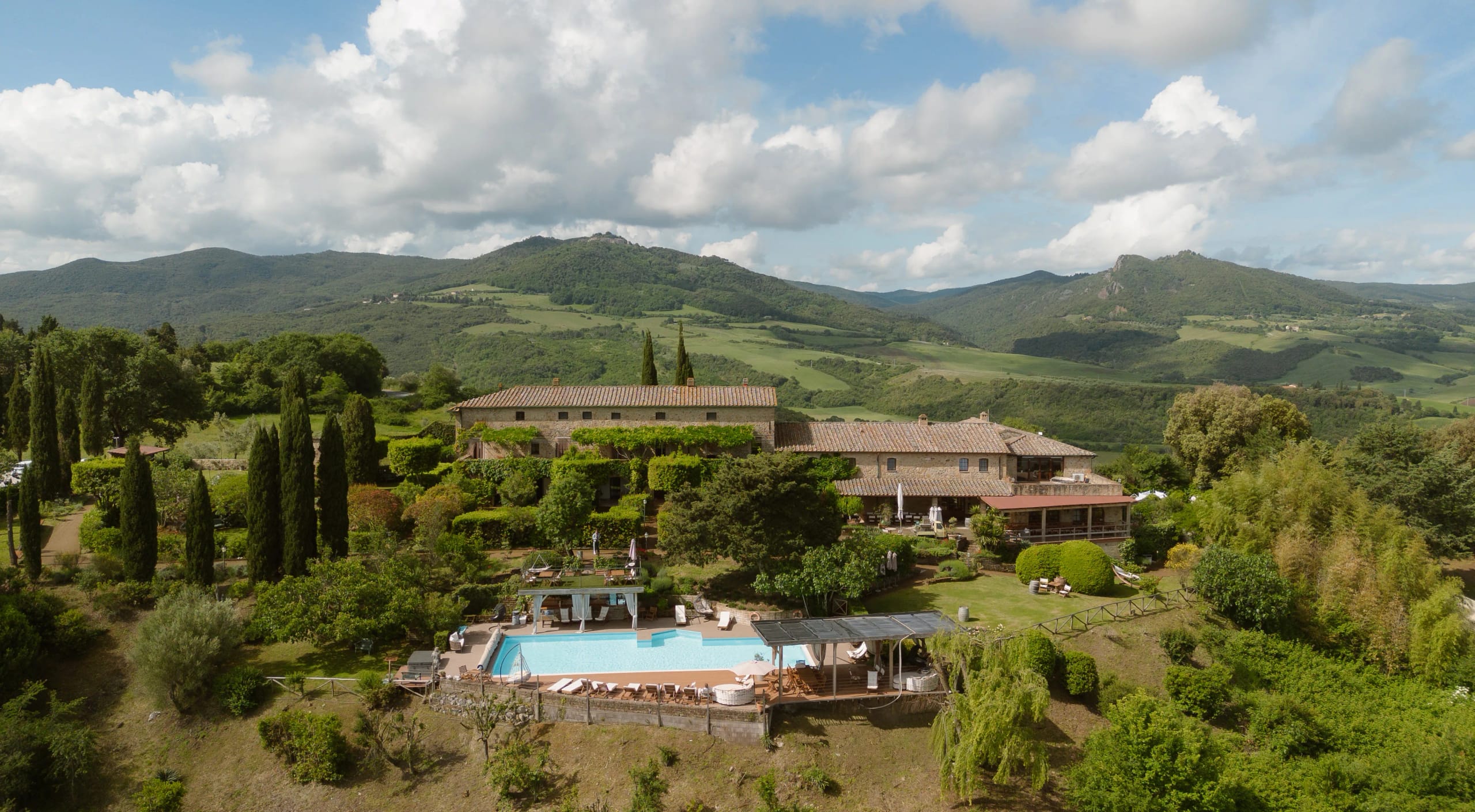 Een prachtig uitzicht op een luxe villa omringd door weelderige groene heuvels in Toscane, compleet met een verfrissend zwembad en zonbedden, perfect voor ontspanning in de natuur.