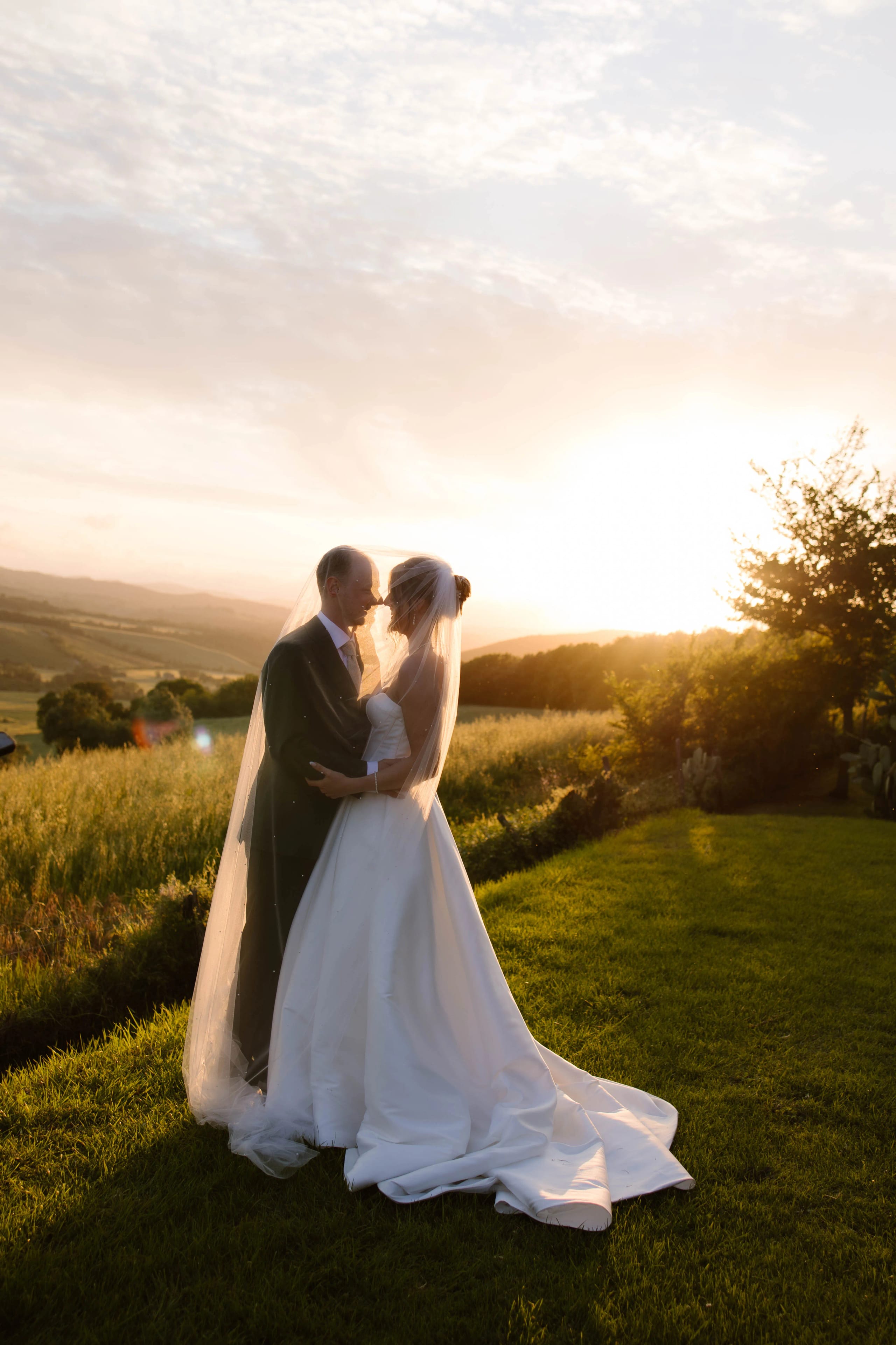Bruidspaar Jari en Julia deelt een intieme kus bij zonsondergang in het prachtige landschap van Toscane - Destination Wedding Italië