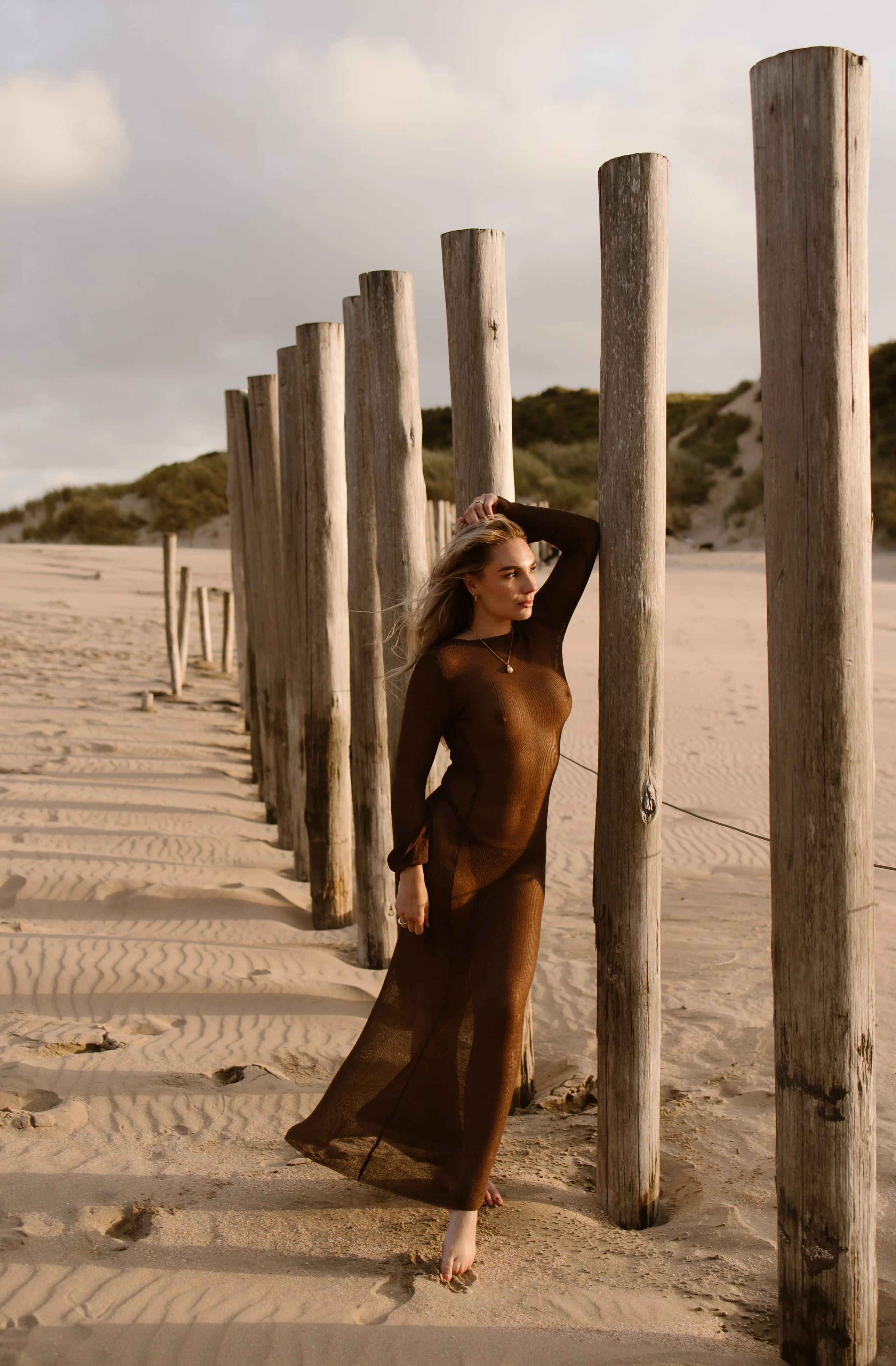 Sammy in lange bruine jurk voor een beach boudoir shoot bij de houten palen in Bloemendaal